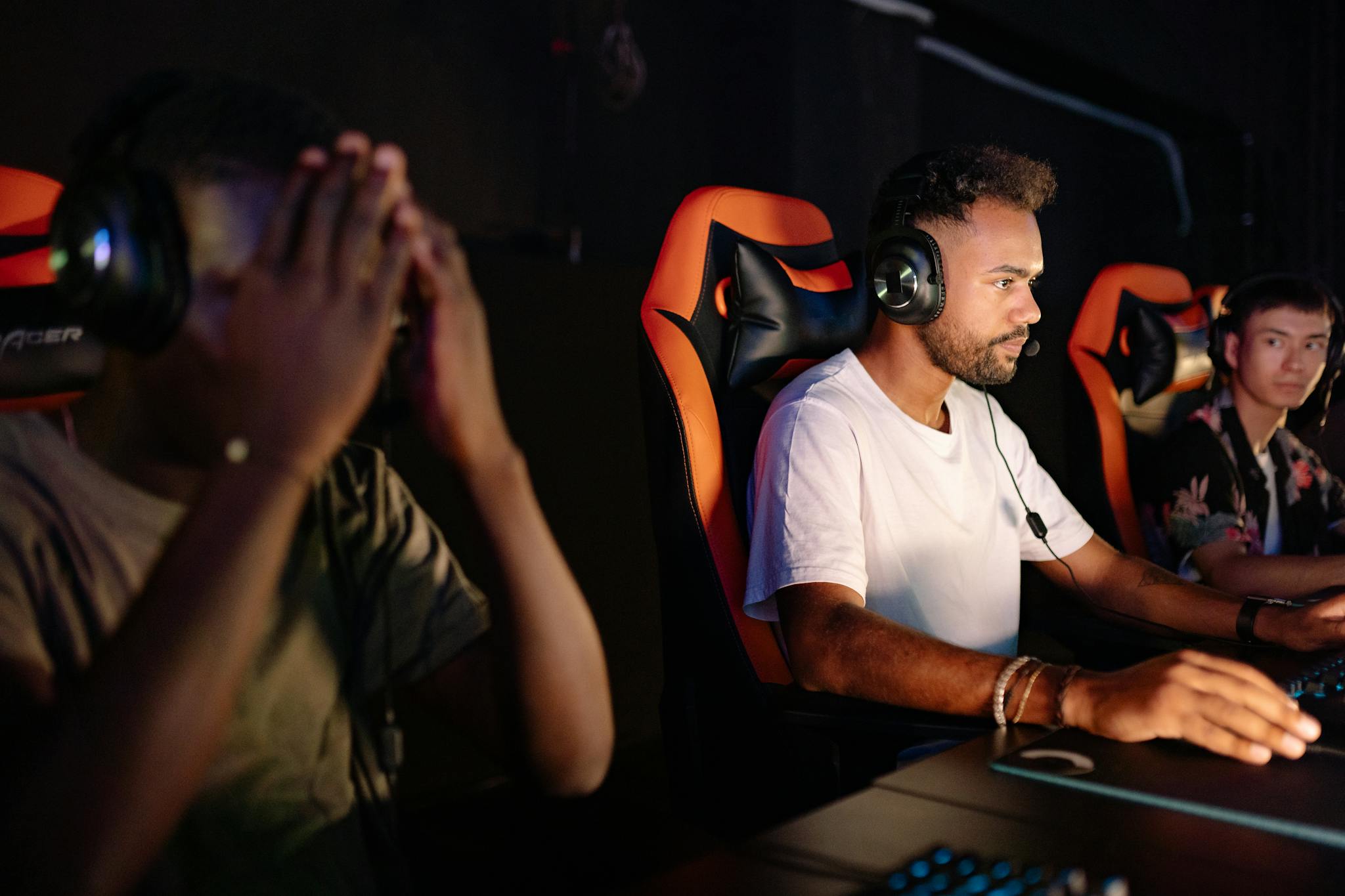 Three young men playing video games in an esports setting with headsets and gaming chairs.
